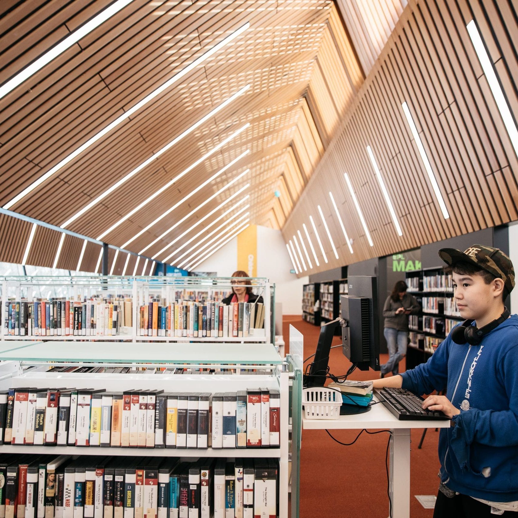 Capilano Branch Customer at Capilano Branch stands beside book stacks and uses a computer