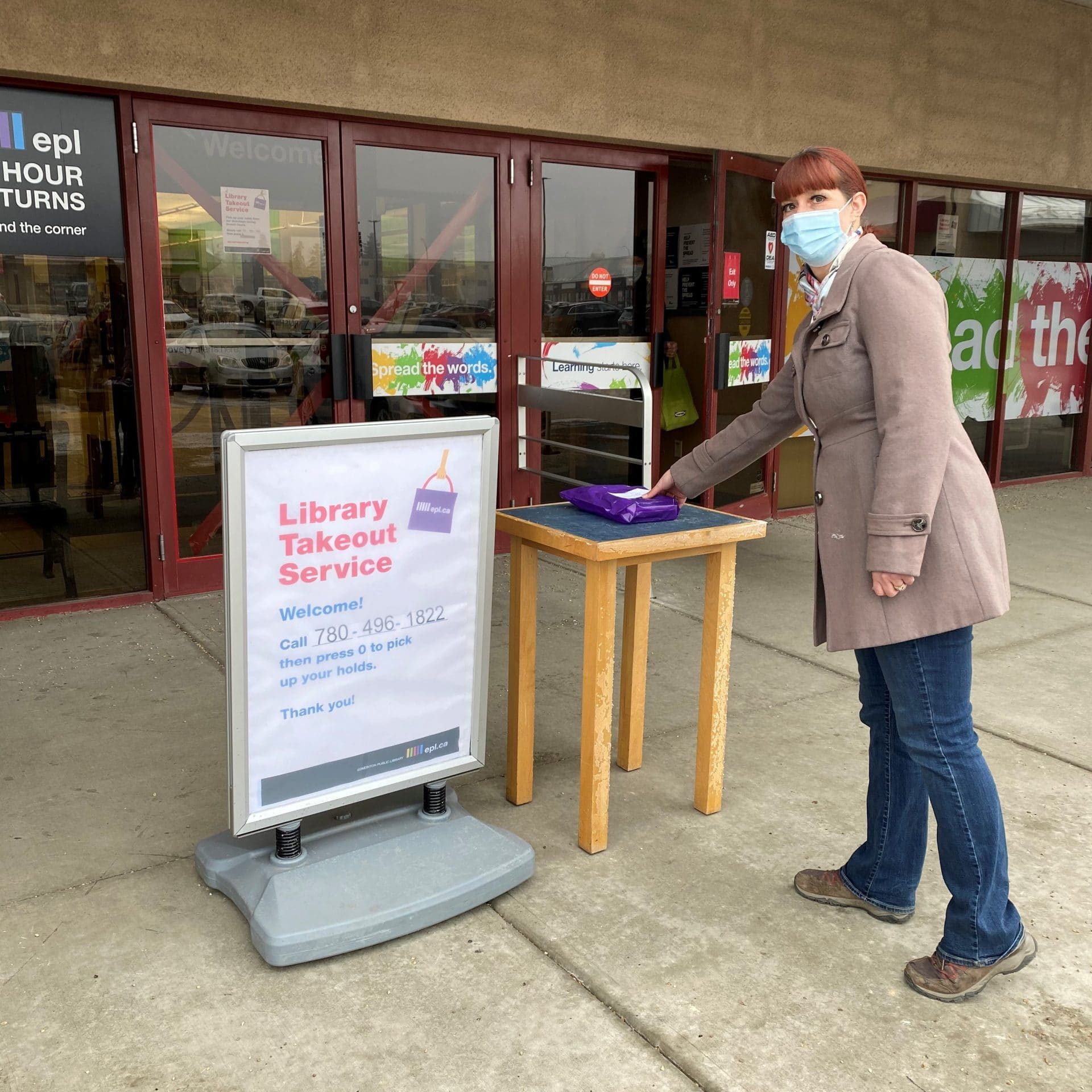 Library Takeout Library staff member wearing a mask placing a customer's books on a table for pick up